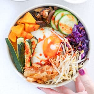 Looking down onto a bowl of bibimbap full of brightly coloured vegetables and a fried egg.