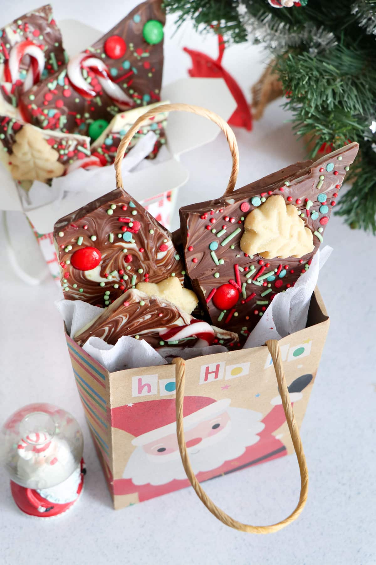 A Christmas gift bag and a gift box are filled with pieces of chocolate bark recipe.