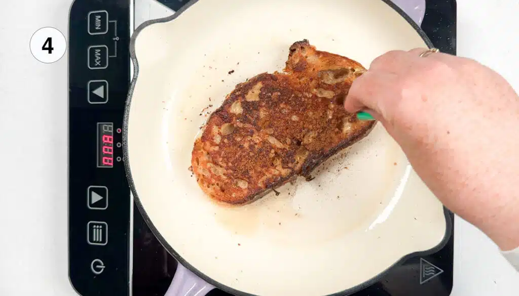 A white hand is sprinkling brown sugar and cinnamon over a piece of french toast in a pan.