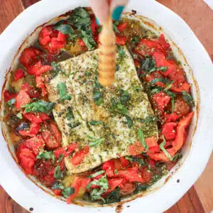 A sizzling dish of baked feta dip with roasted tomatoes is being drizzled with honey.