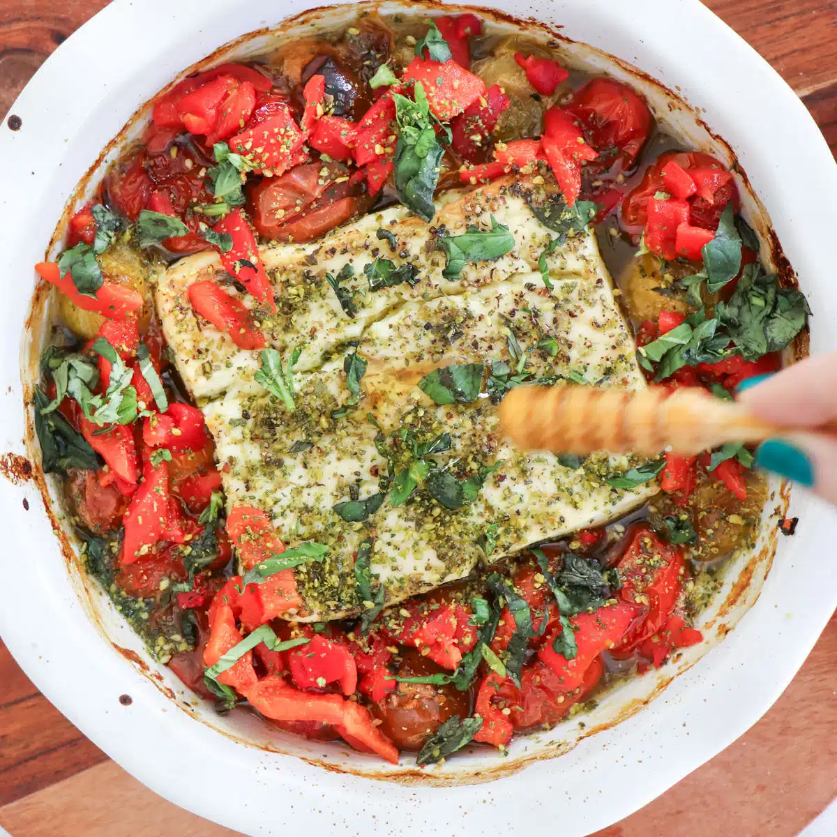 A sizzling dish of baked feta dip with roasted tomatoes is being drizzled with honey.