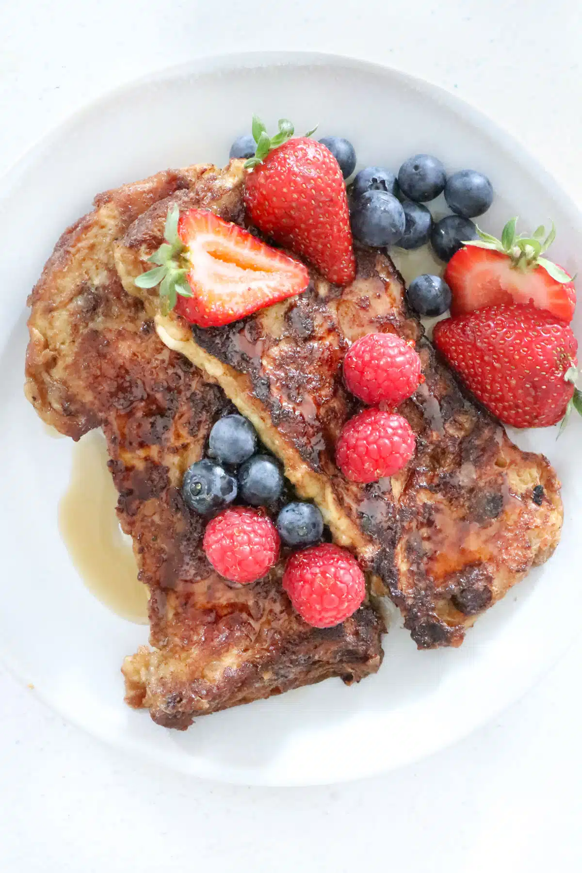 Two slices of panettone french toast are on a plate topped with berries and maple syrup.