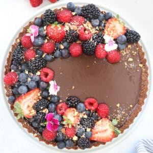 A close up looking down onto a raw chocolate tart that's been decorated with berries and flowers.