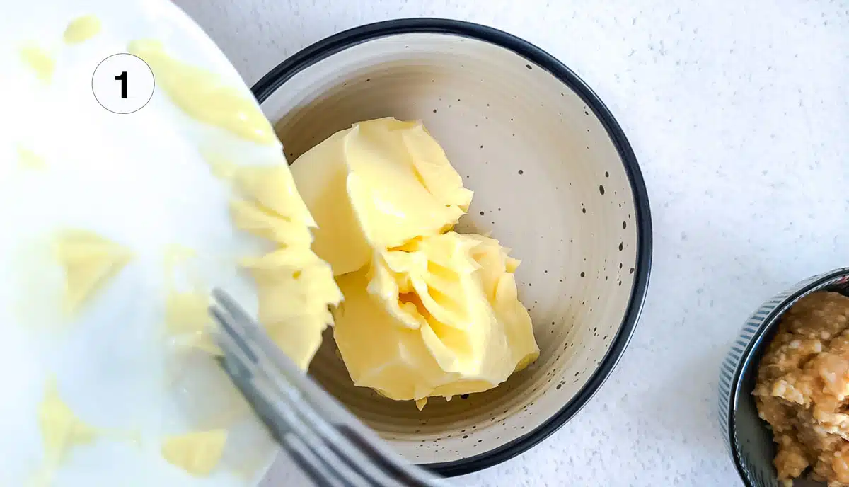 Butter is being tipped off a small plate into a bowl.