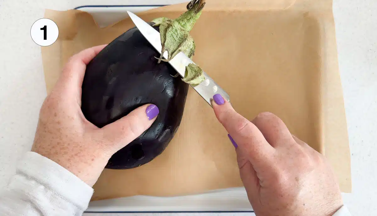 The green leaves are being cut off the top of a large globe eggplant.