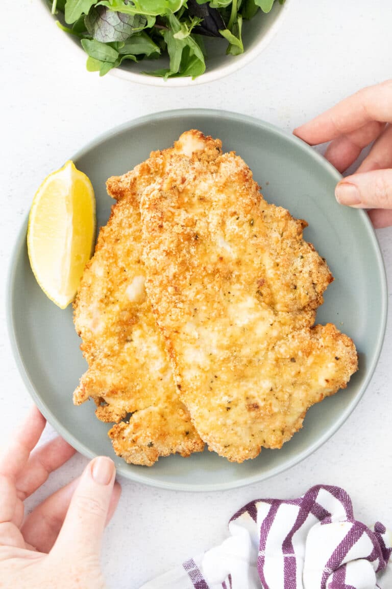 Two golden air fryer chicken cutlets are stacked on a grey plate with a lemon wedge beside them.