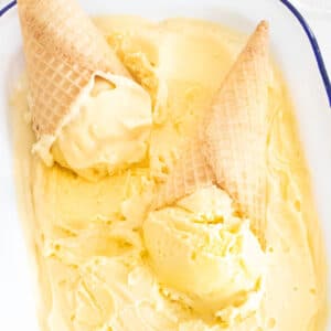 Mango Ice Cream is scooped into two cones that are sitting upside down in the remaining tub of ice cream.