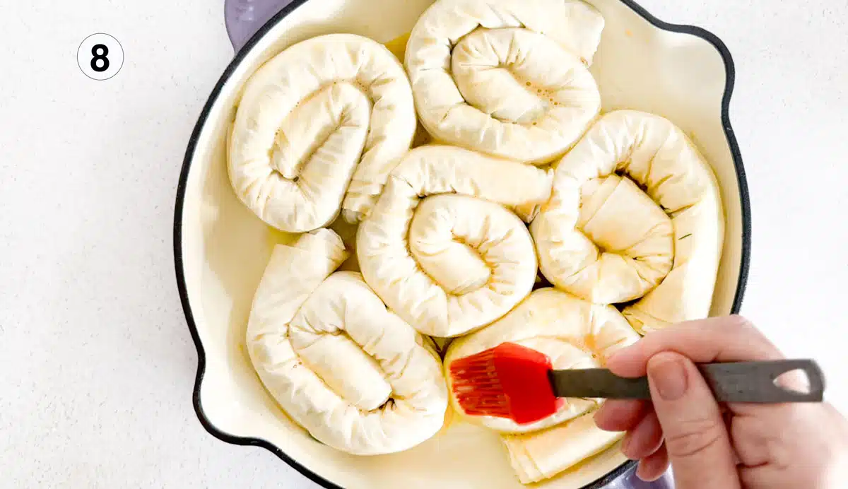 Egg wash is being brushed over filo spirals filled with leek and feta mixture.
