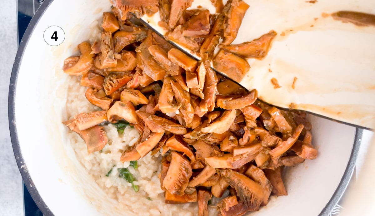 Pouring cooked pine mushrooms onto a finished risotto in a large pot.
