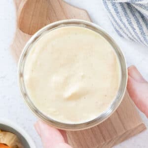 A small jar of kimchi mayo is being held by a white hand.