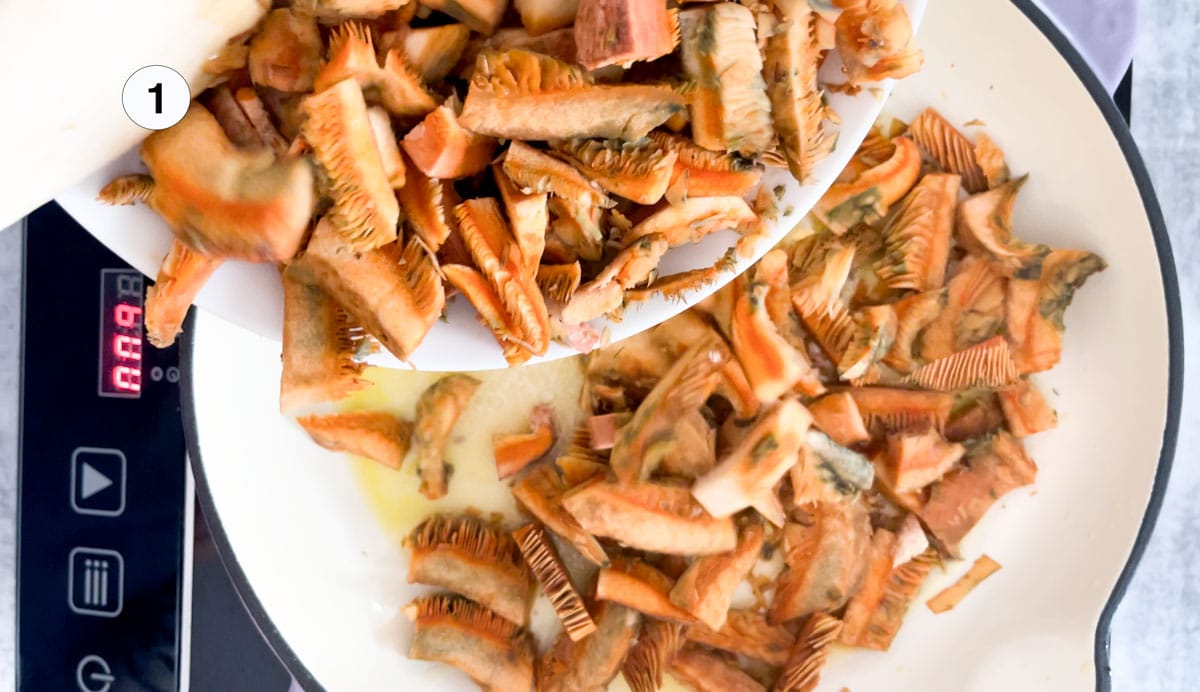 Bright orange pine mushrooms are sautéing in a pan with butter and oil.