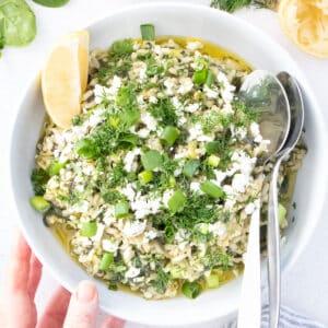 A large white bowl is filled with Spanakorizo, topped with feta, dill and scallions and drizzled with olive oil.