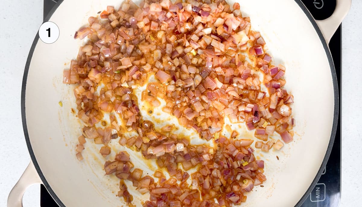 Onion, olive oil, and harissa are being stirred together in a large pot for the base of a vegan curry.