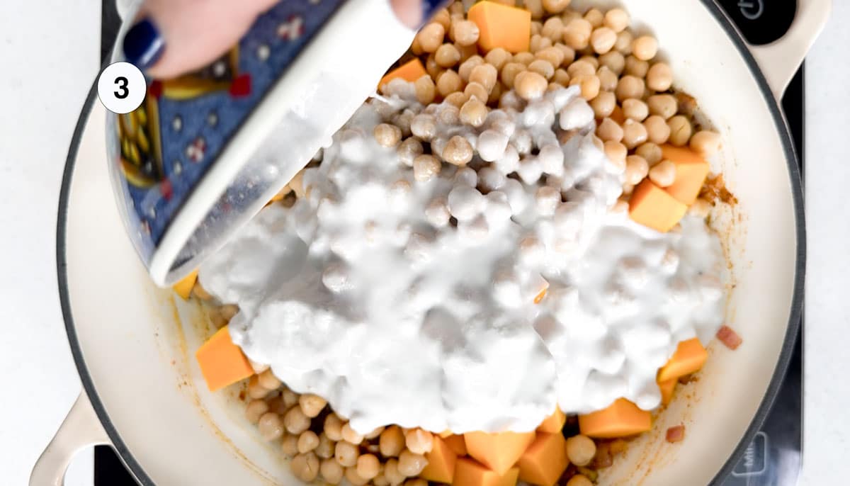 Chickpeas, pumpkin, and coconut milk have been poured into a large pot of chickpea spinach curry.