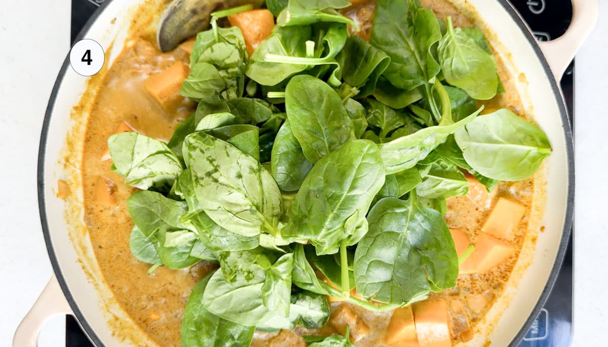A large handful of bright green baby spinach has been added to the top of a curry to be stirred through.