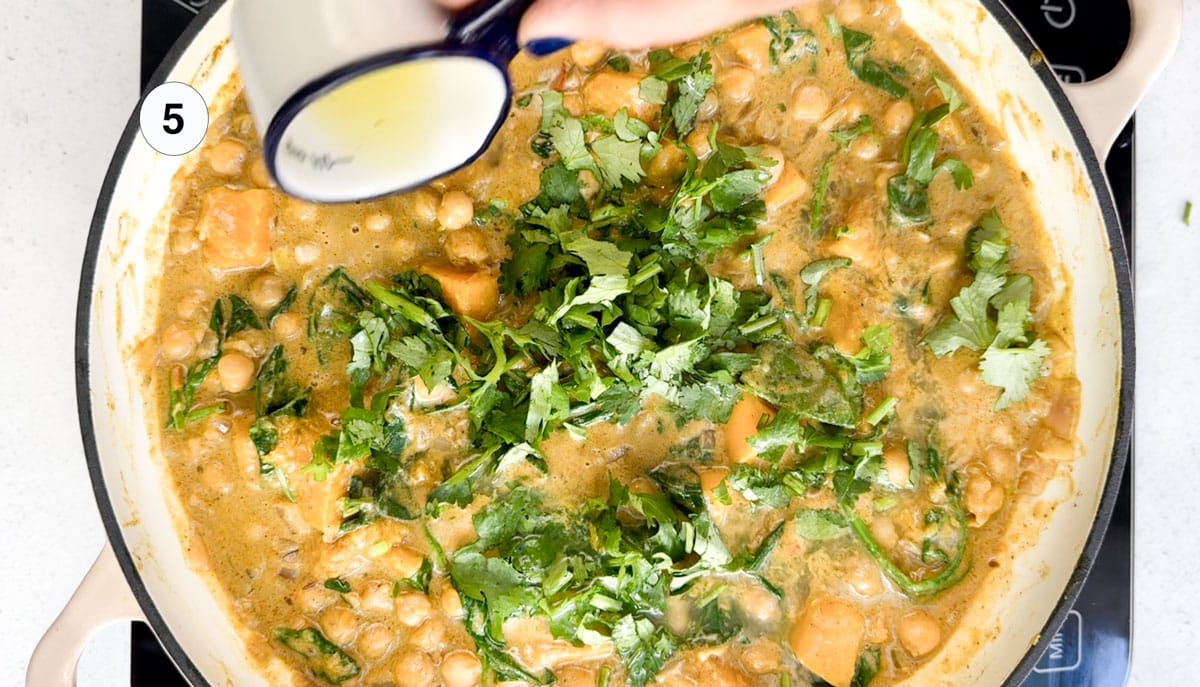 A white hand is pouring lime juice over the top of a vegan chickpea curry.