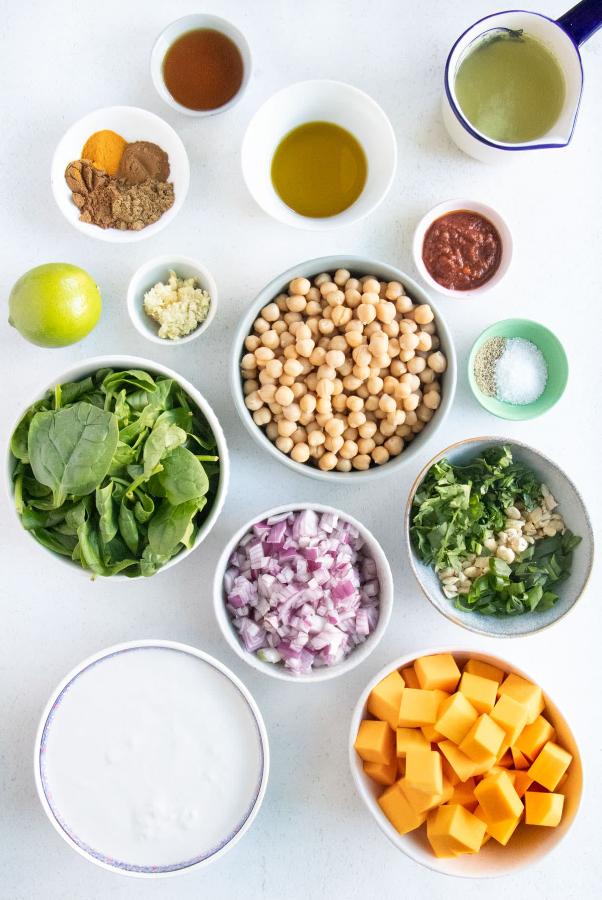 All the ingredients needed to make Chickpea Spinach Curry are laid out across a table in small bowls.