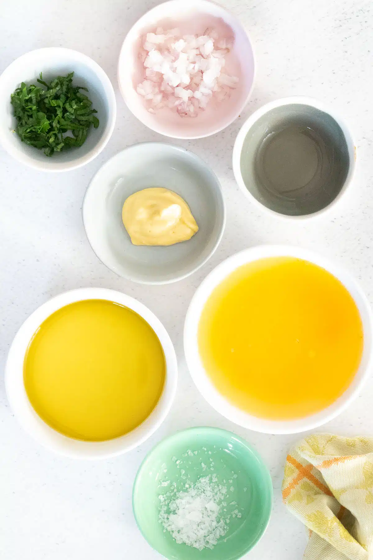 All the ingredients needed to make orange vinaigrette have been laid out across a table in small bowls.