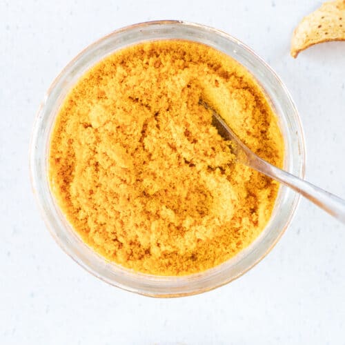 A small jar of mandarin peel powder with a spoon dipped into it is sitting on a white table top.