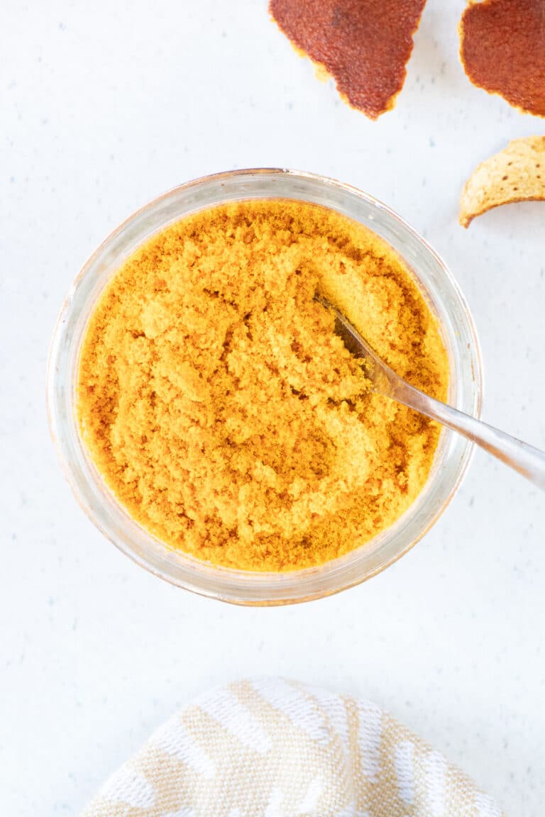 A small jar of mandarin peel powder with a spoon dipped into it is sitting on a white table top.