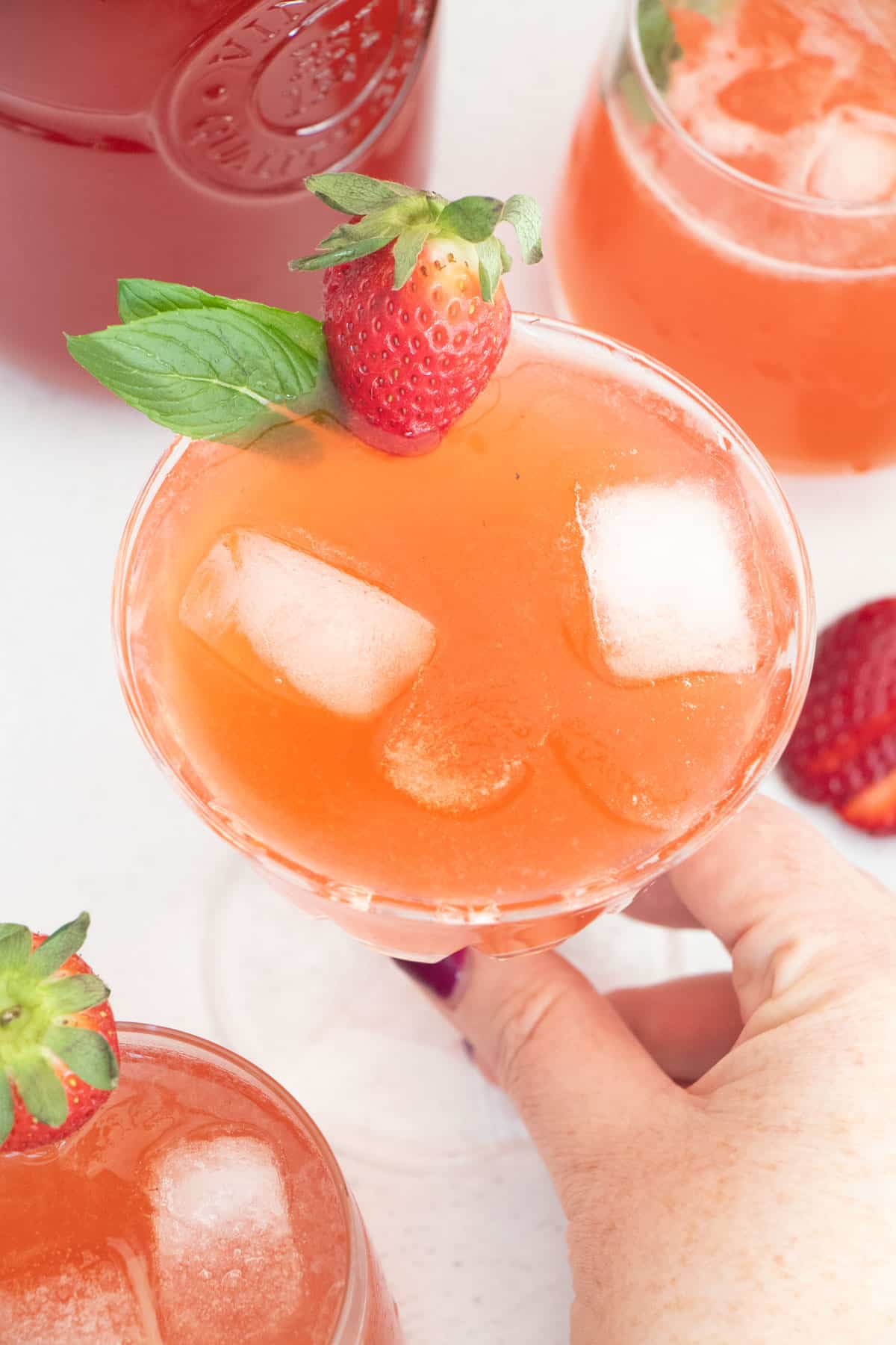 A white hand is holding a vintage glass full of pink strawberry shrub and mineral water.