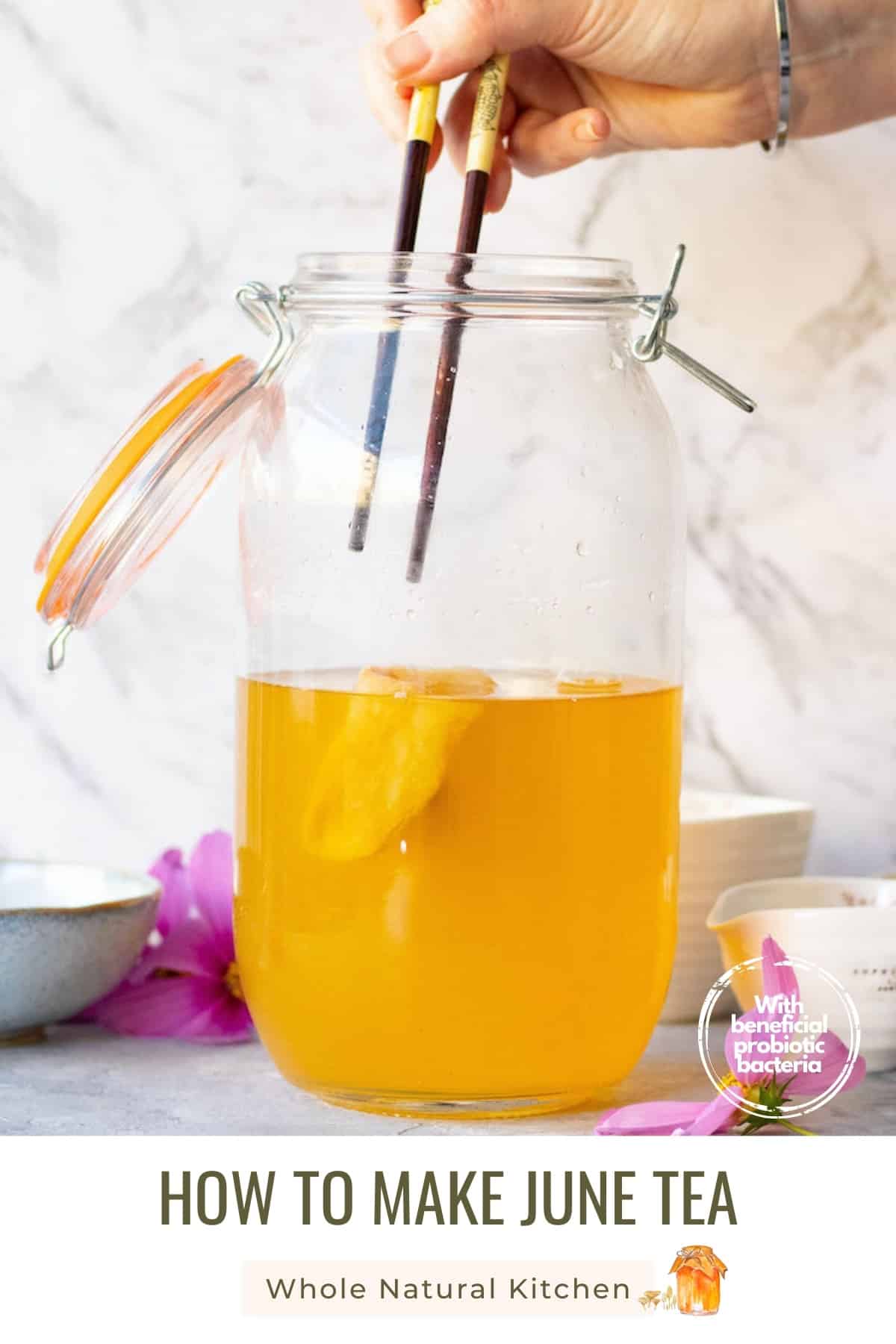 A white hand is putting chopsticks into a large jar to stir the jun tea and jun scoby.
