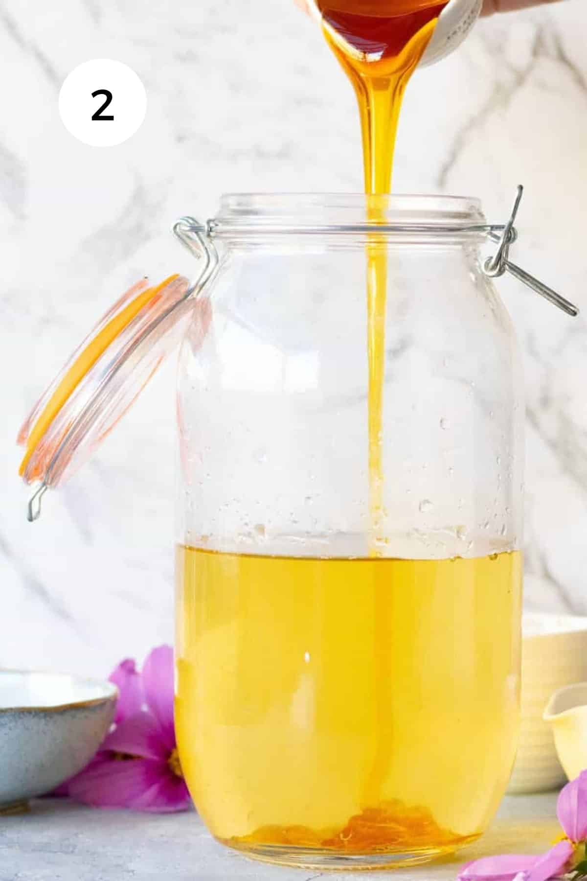 Pouring honey into a large jar of golden, fermented jun tea.