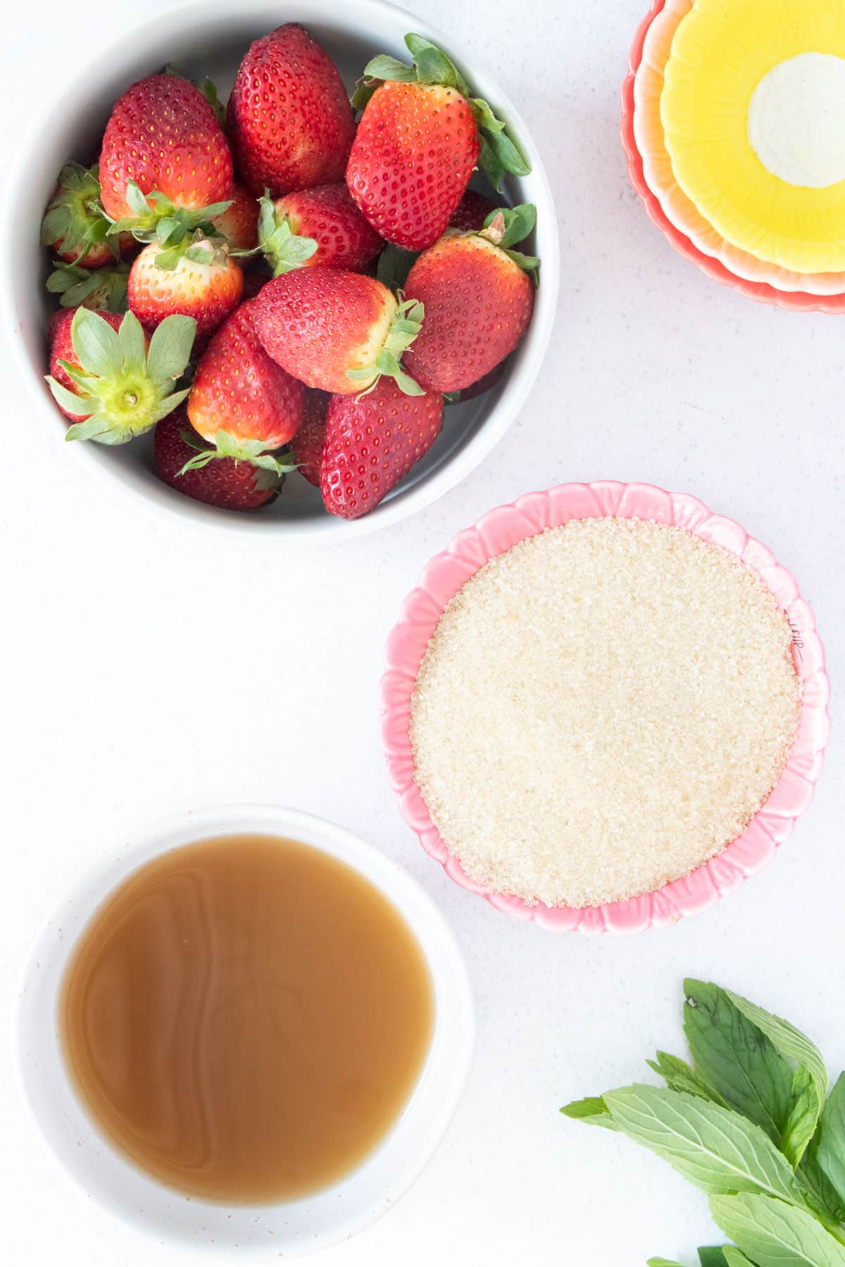 All the ingredients needed to make a strawberry shrub are laid out across a white table top.