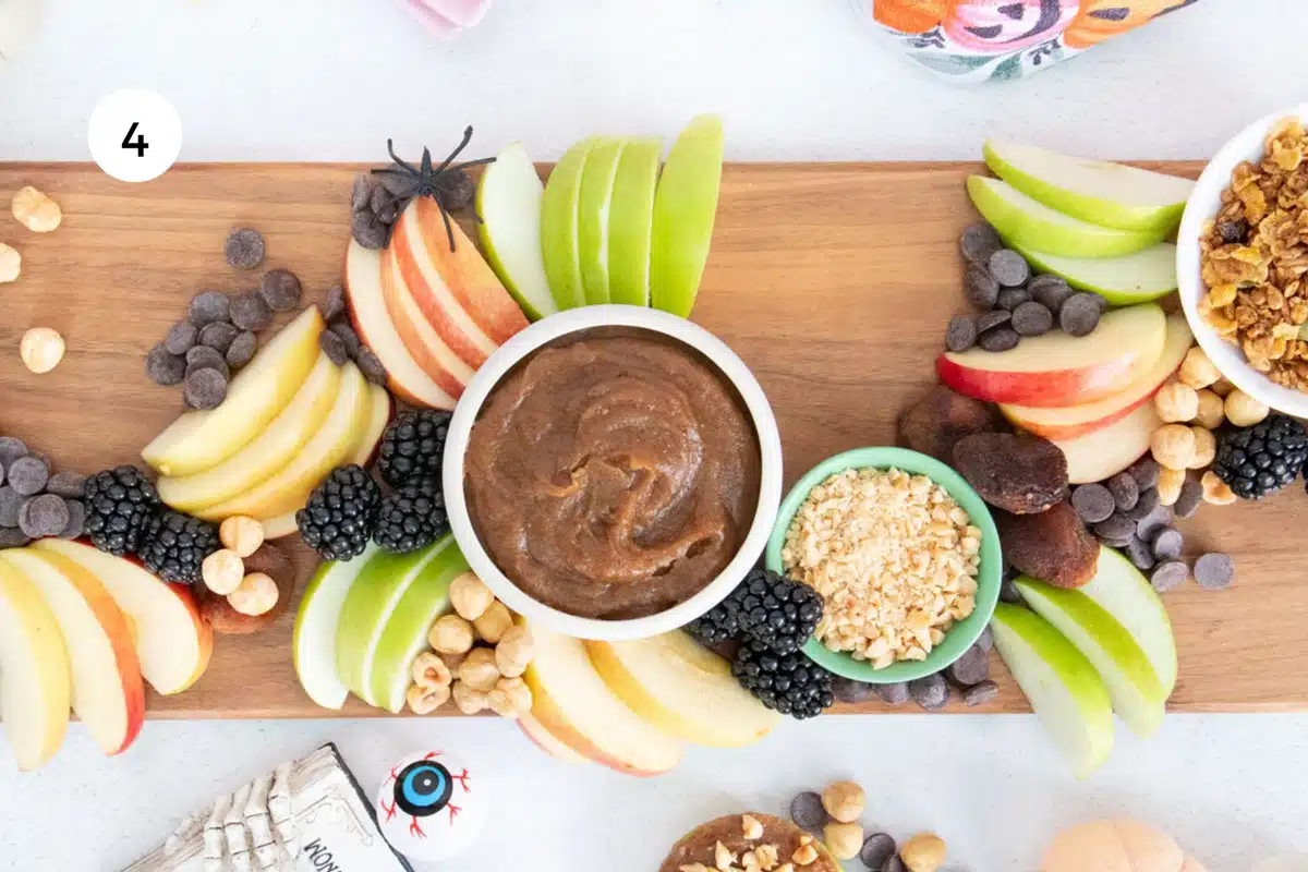 Blackberries and dried fruit are being added to sweet dips and apple slices on an caramel apple dessert board.