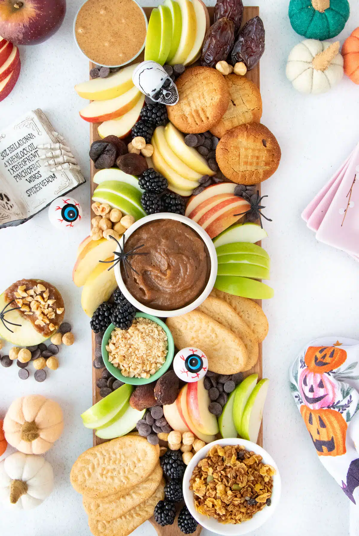 Looking down over a large rectangular caramel apple charcuterie board with Halloween decorations beside it.