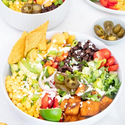 A large taco bowl is filled with black beans, corn, sweet potato, bell pepper, avocado and mango salsa.