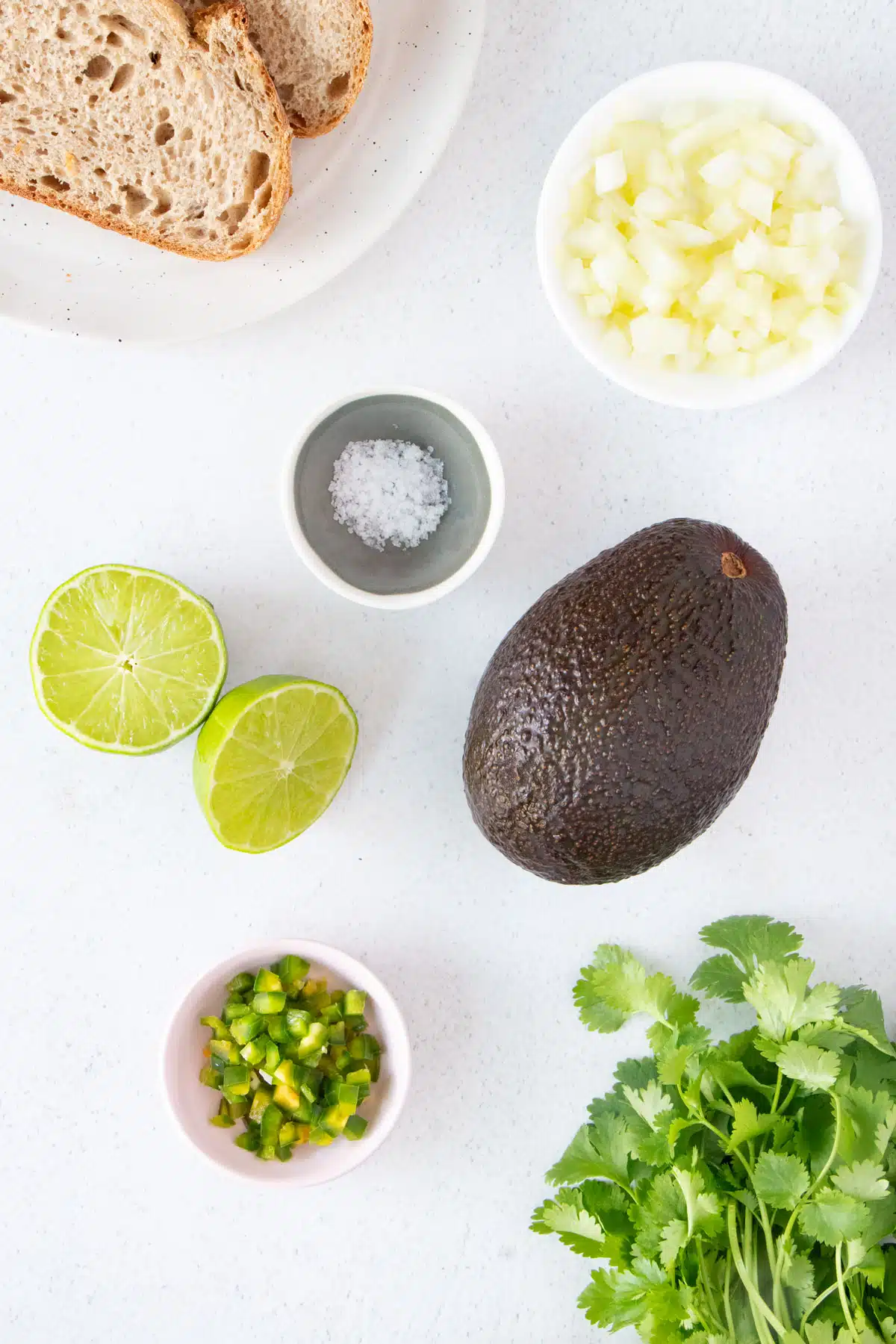 All the ingredients needed to make guacamole toast are laid out across a white kitchen bench.