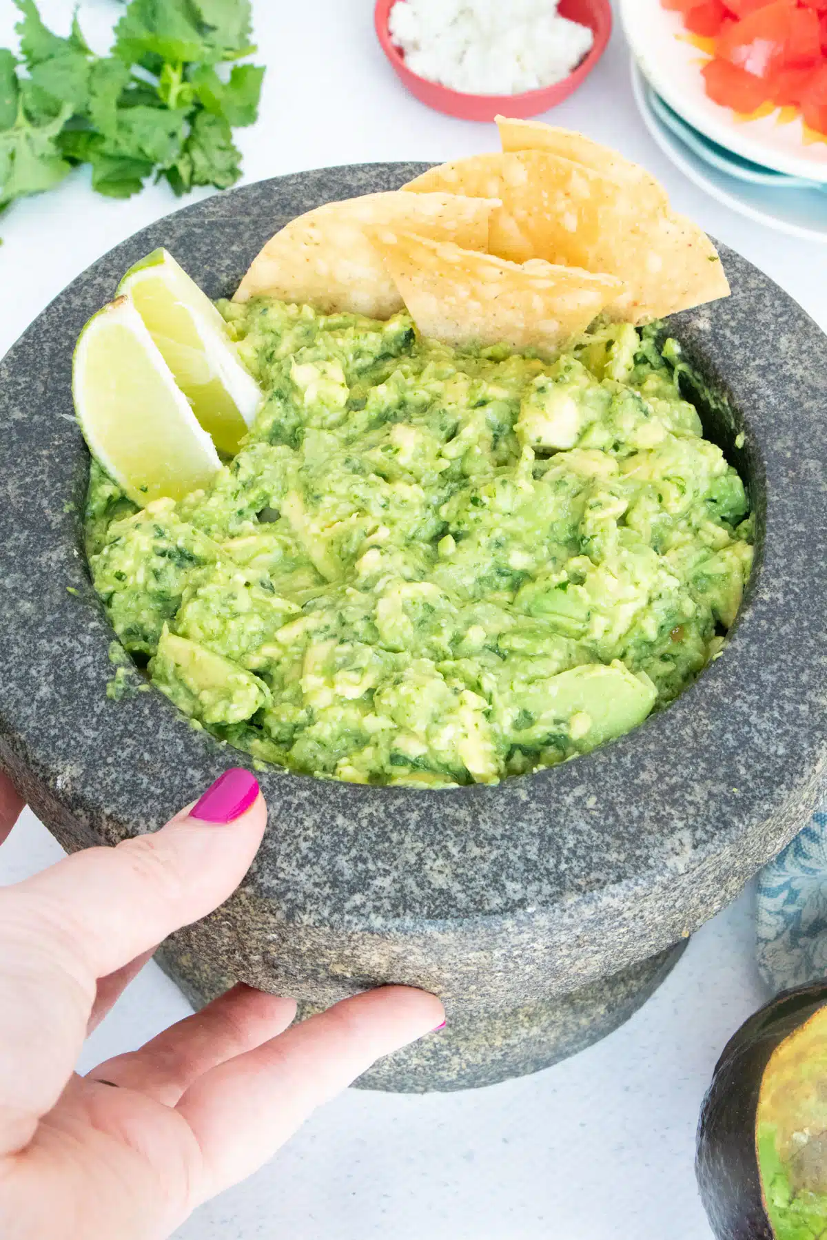 Guacamole fills a large stone mortar to the brim. Corn chips and lime wedges have been added to the top.
