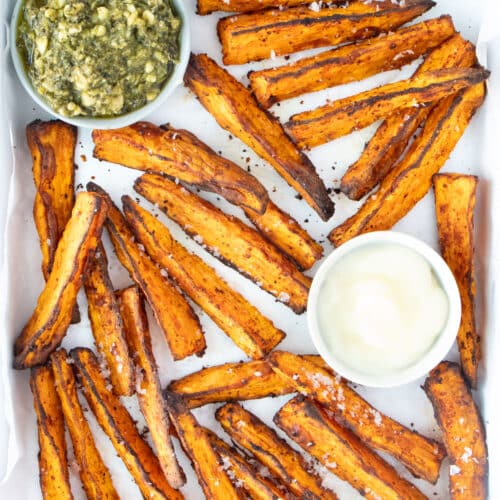 Golden brown air fryer sweet potato wedges are spread out on a white tray with two interspersed dips.