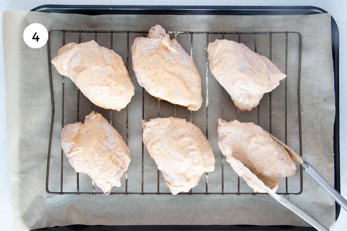 Yogurt Marinated Chicken pieces are being placed onto a wire rack with silver tongs.