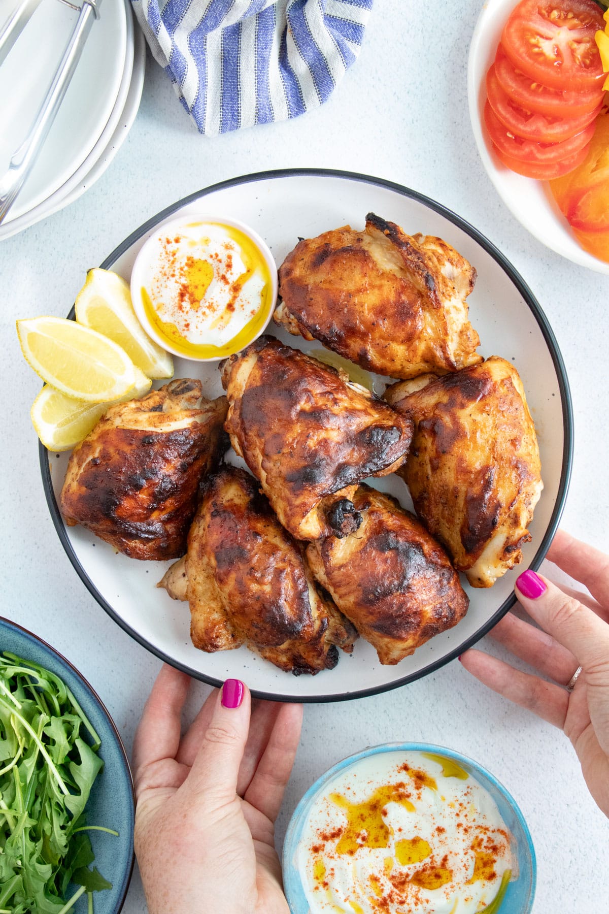 Two white hands are placing a plate full of yogurt marinated chicken down onto a table.