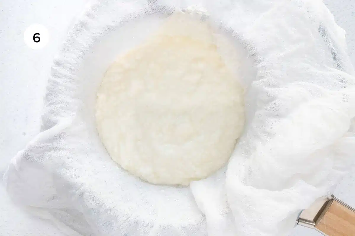 Yoghurt has been poured into a strainer lined with white cheesecloth.