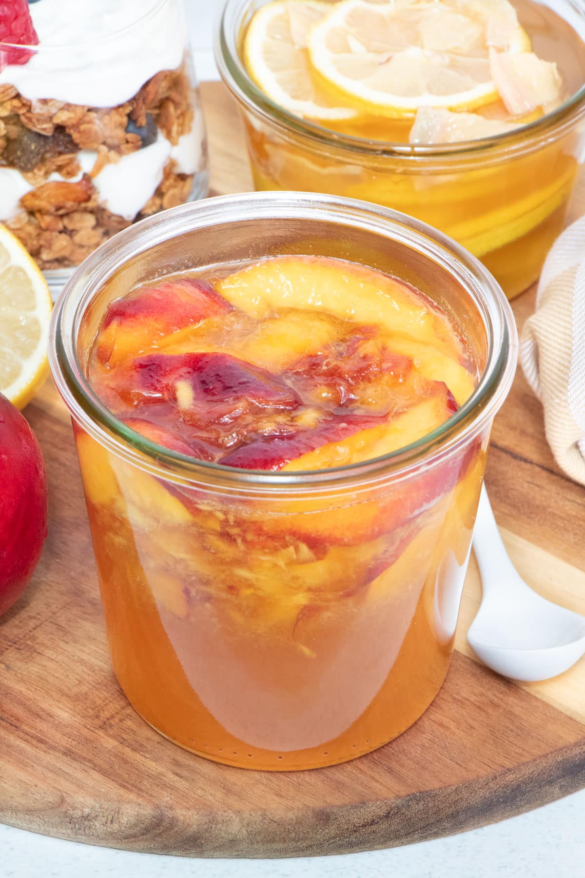 A jar of fermented fruit is sitting on a wooden serving board. Another of fermented lemon and ginger honey sits behind.