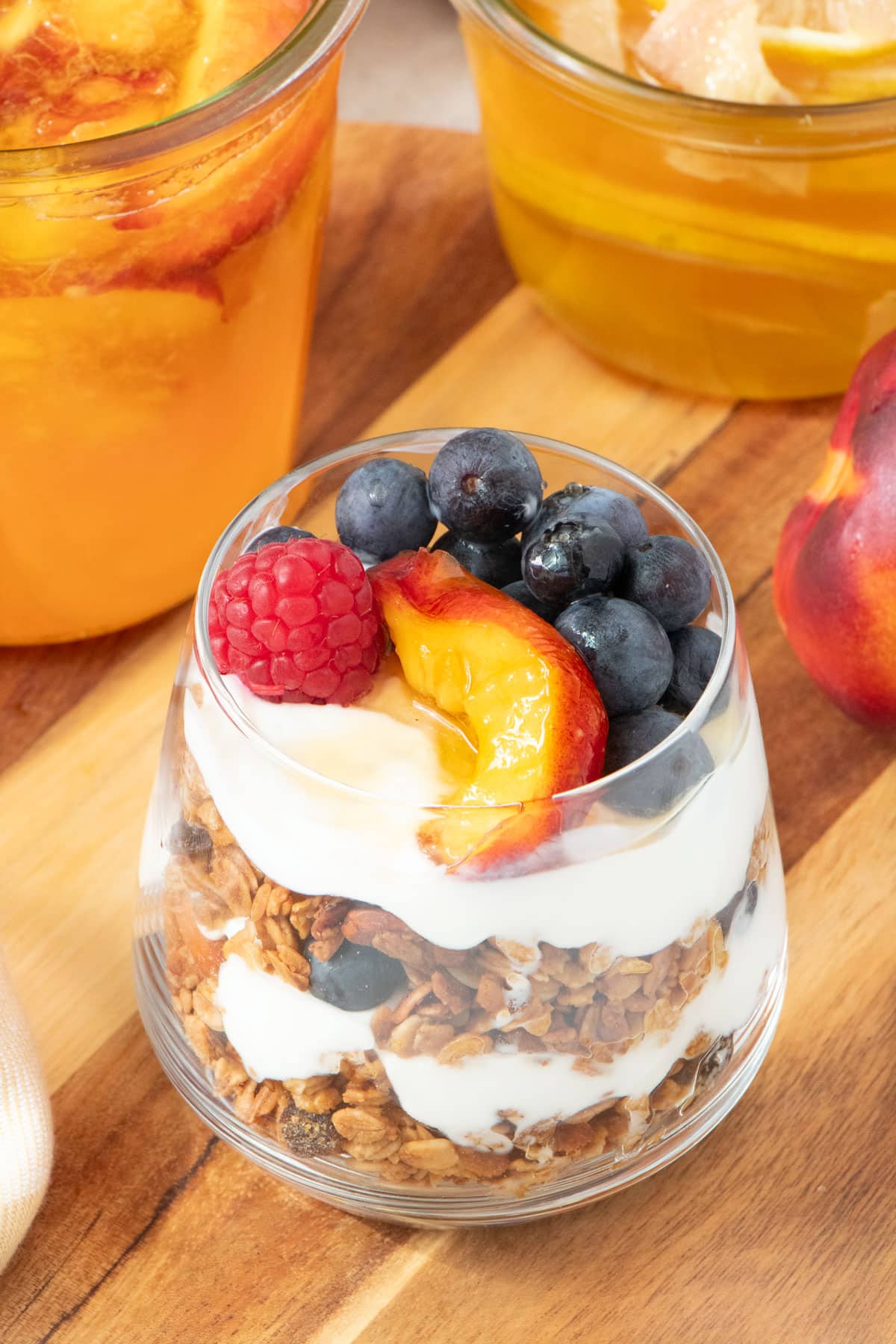 A small glass is filled with layers of granola and yoghurt and is topped with fermented fruit plus a drizzle of honey.