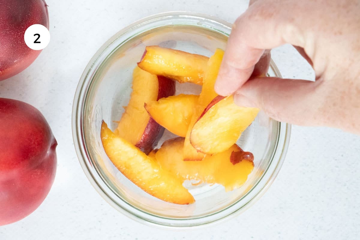 A white hand is adding slices of nectarine to a large glass jar.