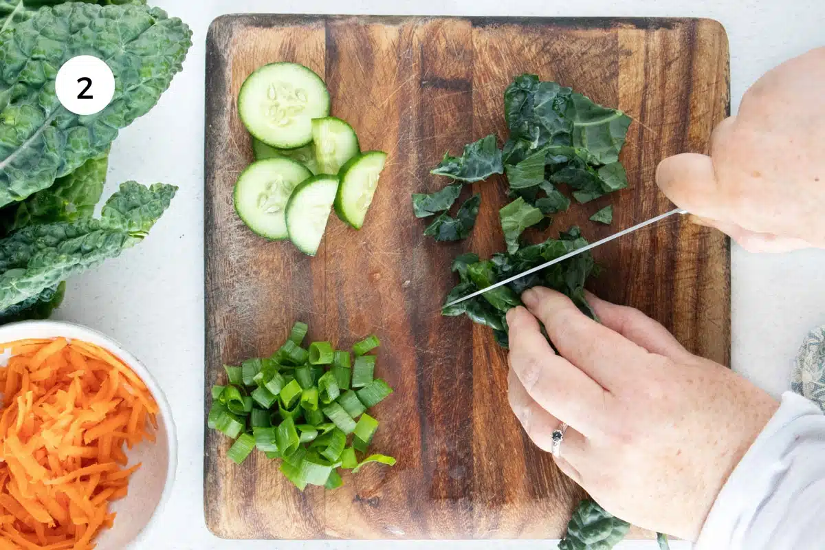 A white hand is chopping kale on a wooden chopping board with a large silver knife.
