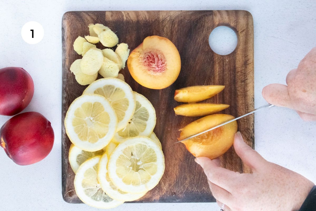 A white hand is holding a nectarine on a chopping board while the other hand slices through it with a large knife.
