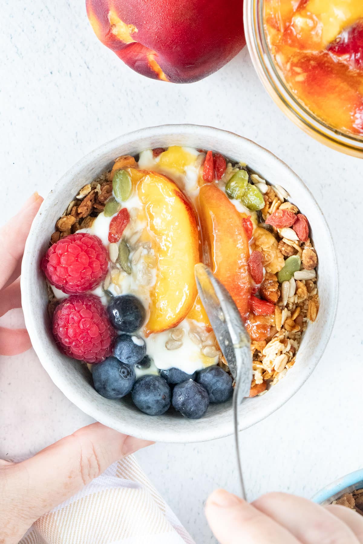 A small bowl of yoghurt and granola is topped with berries, fermented fruit, and a drizzle of honey.