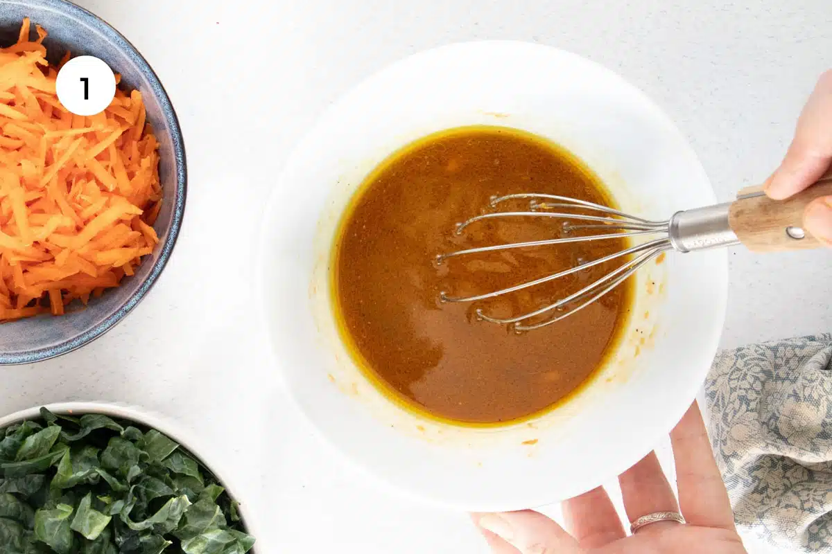 Miso dressing is being whisked together in a large white bowl.