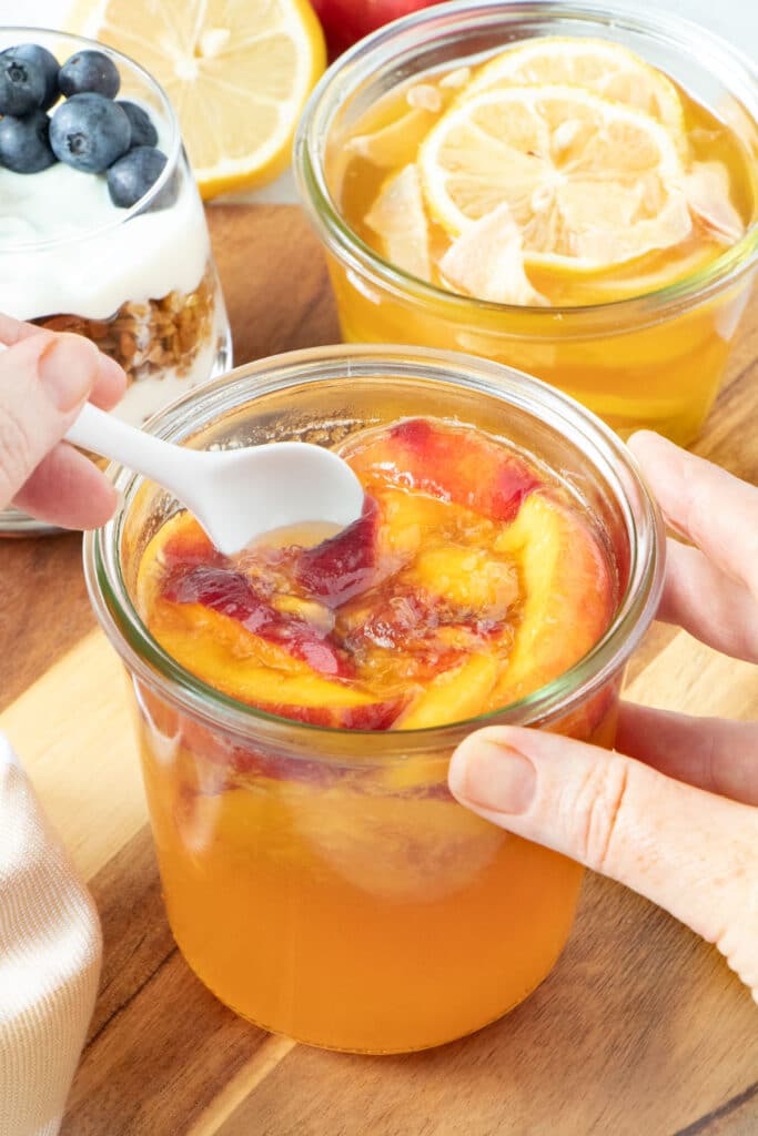 A white hand is scooping honey fermented fruit out of a jar with a small white spoon.
