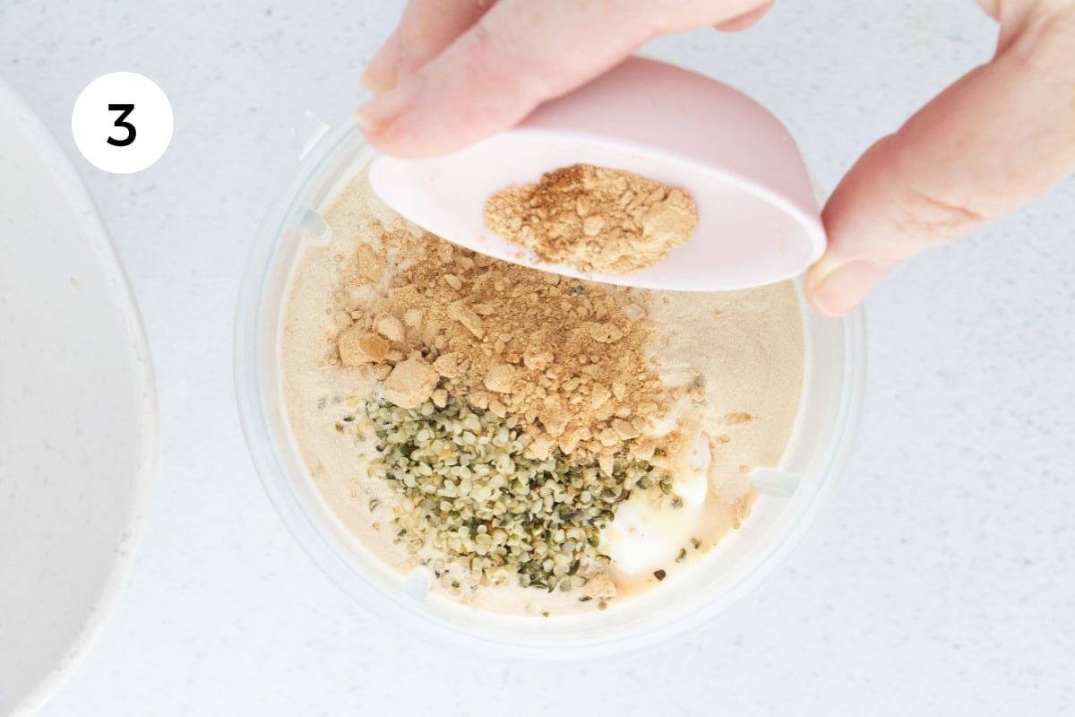 Adding maca powder and cinnamon on top of other ingredients in a blender to make a fruit smoothie.