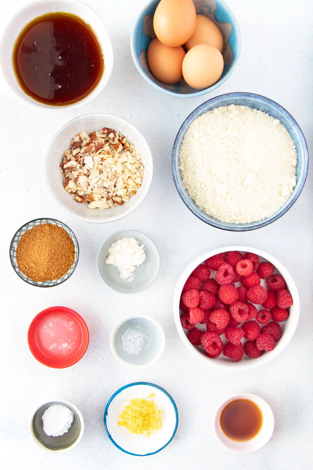 All the ingredients needed to make an almond and raspberry cake are laid out across a table in small bowls.