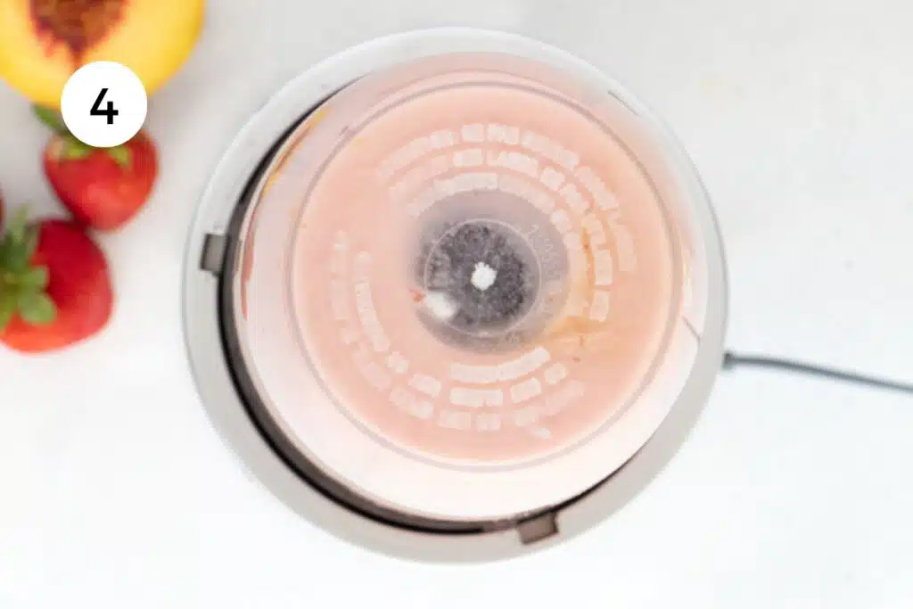 Blending a strawberry and peach smoothie together in a small blender.