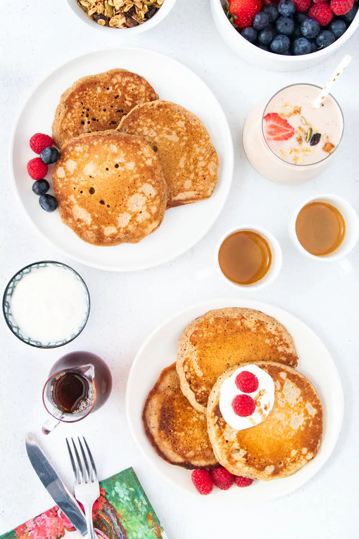 A breakfast table is set with two plates of gluten free dairy free pancakes, two coffees, a smoothie and a bowl of berries.