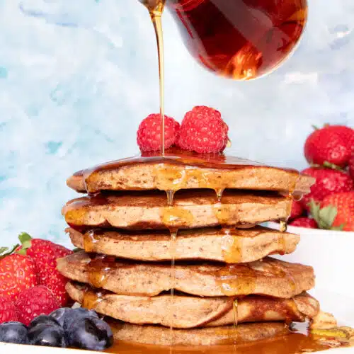 A large stack of Gluten Free Dairy Free pancakes is sitting on a white plate and being drizzled with maple syrup.
